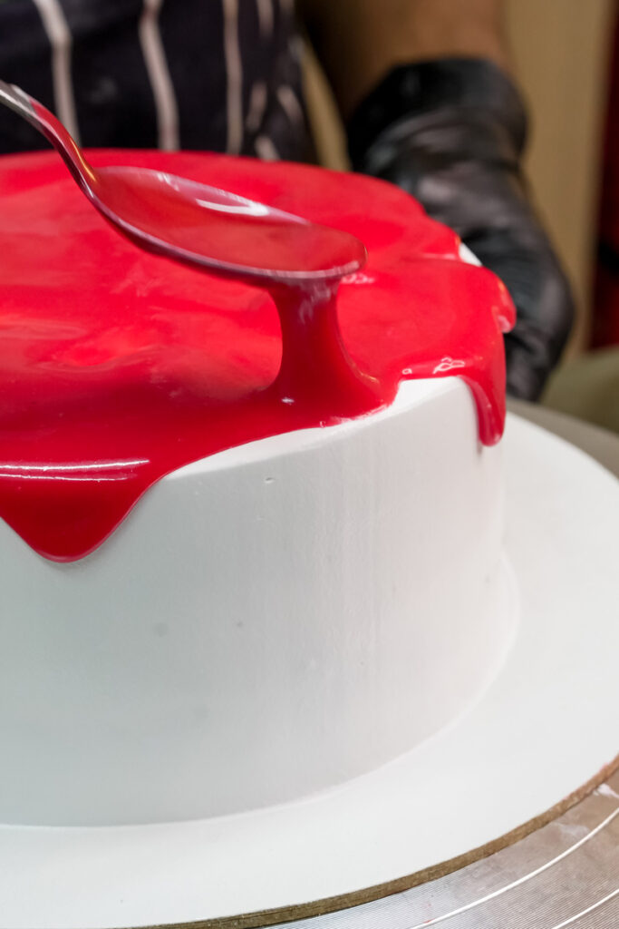 A close-up of red glaze dripping down the side of a white frosted cake