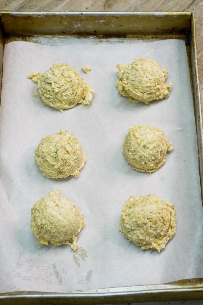 Six uniform scoops of oatmeal cookie dough arranged on a baking sheet, ready for the oven