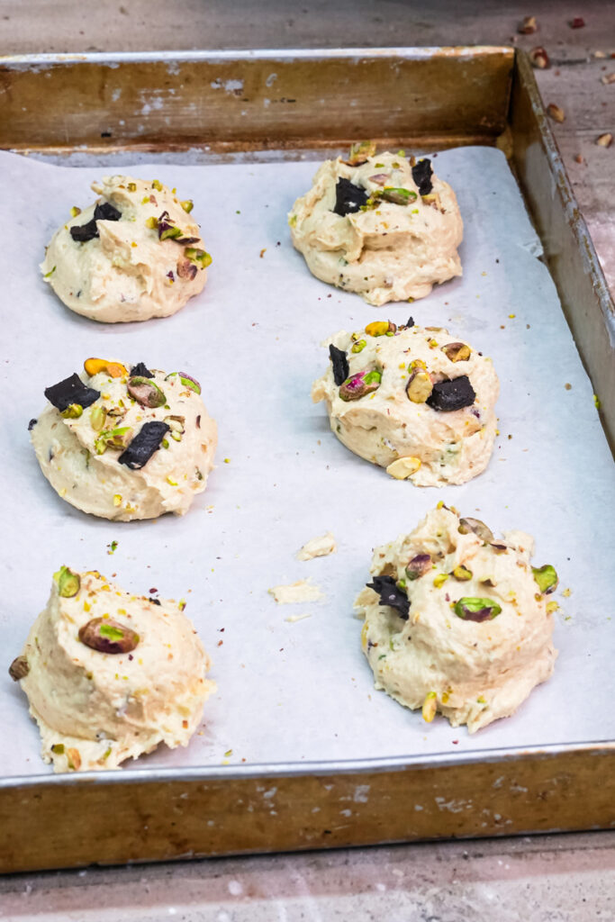 Six scoops of pistachio cookie dough with dark chocolate chunks on a baking sheet