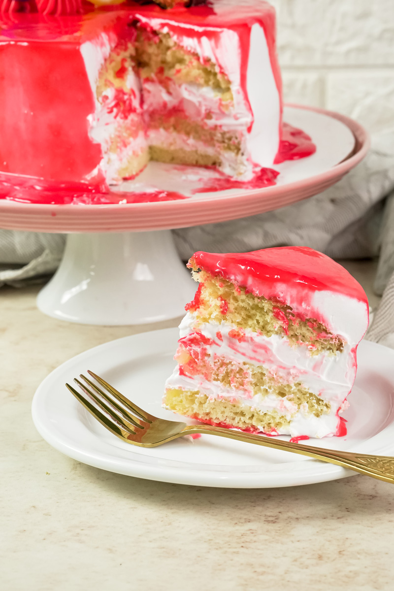 A close-up of a slice of red drip cake with a fork, showing the sponge and cream layers