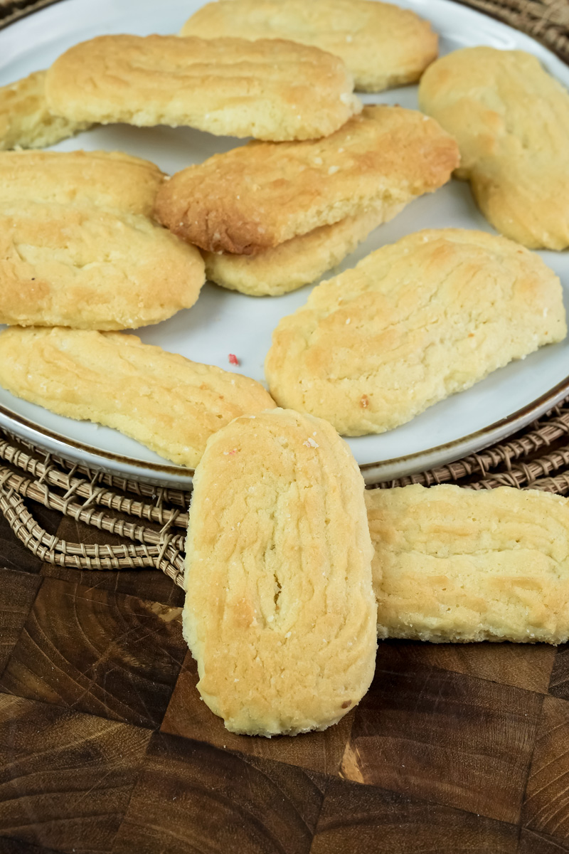 A front-facing shot of a spritz cookie standing upright in front of a plate of other cookies