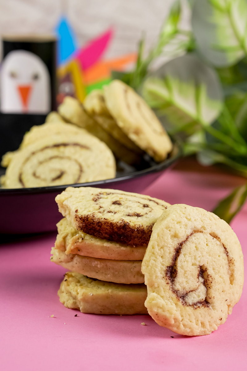 A stack of cinnamon roll cookies with a single cookie leaning against it on a pink surface