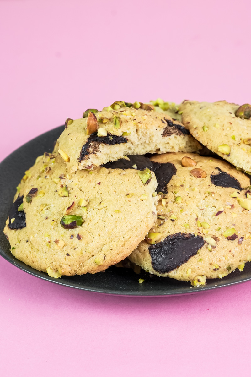 A stack of fresh-baked pistachio cookies with one broken in half to show the inside