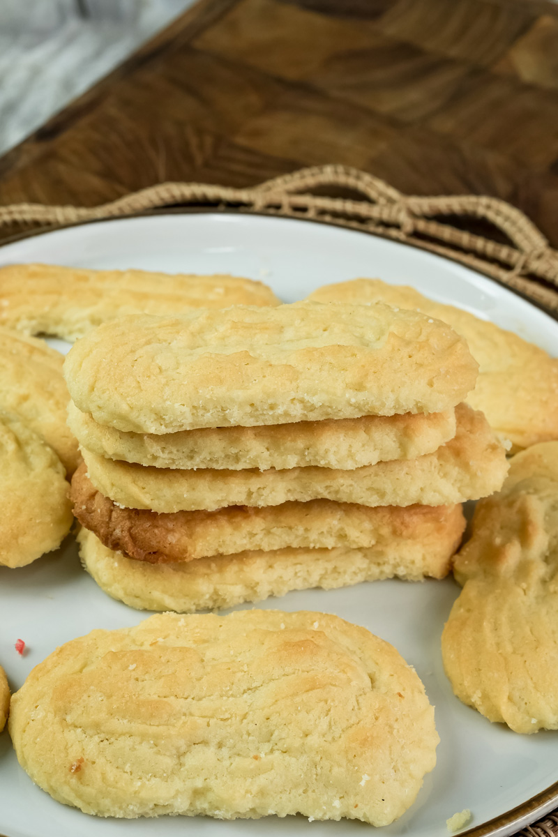 A stack of baked spritz cookies on a plate, with a glass of milk in the blurred background