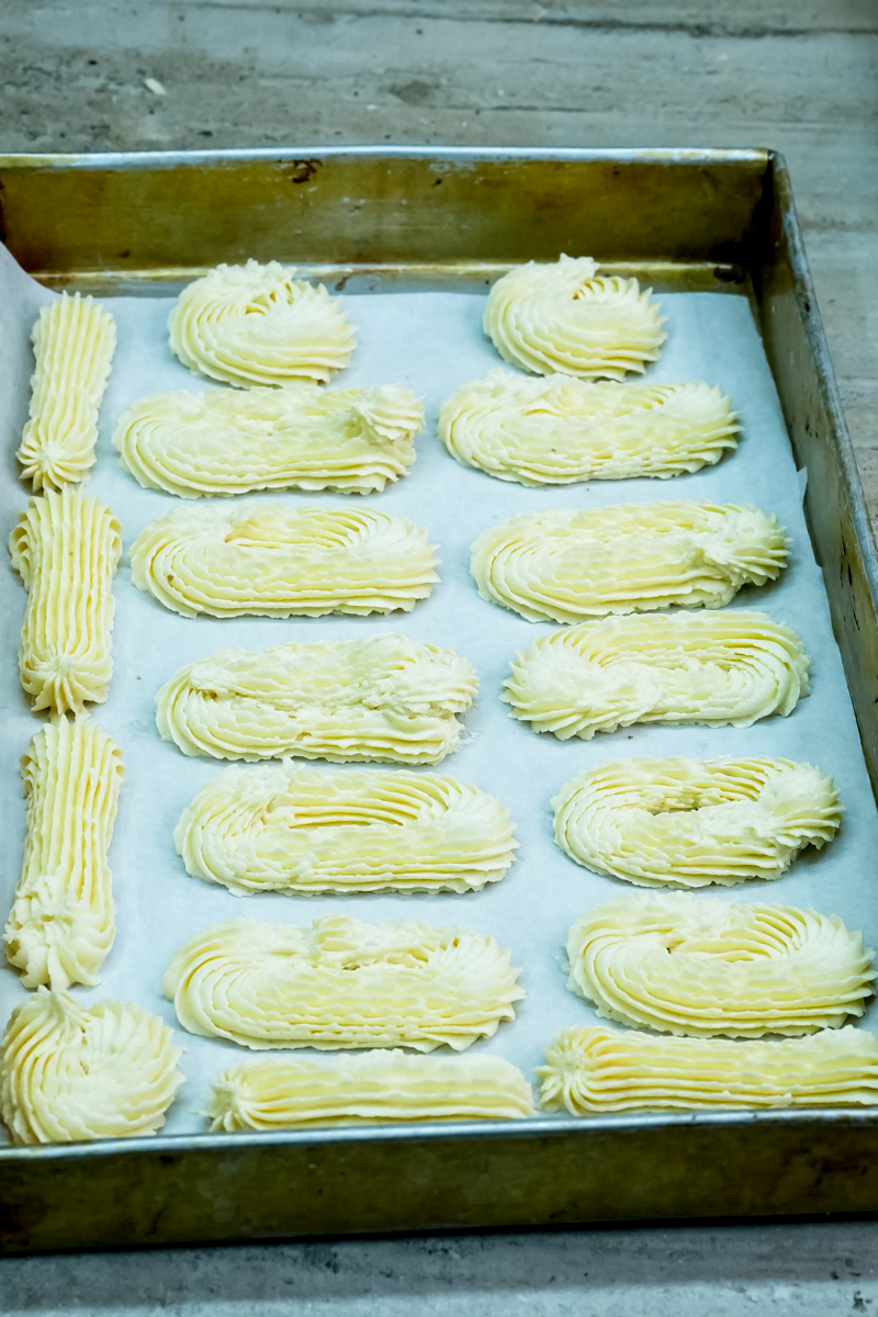 A top-down shot of unbaked spritz cookies piped onto a baking sheet, showcasing different shapes
