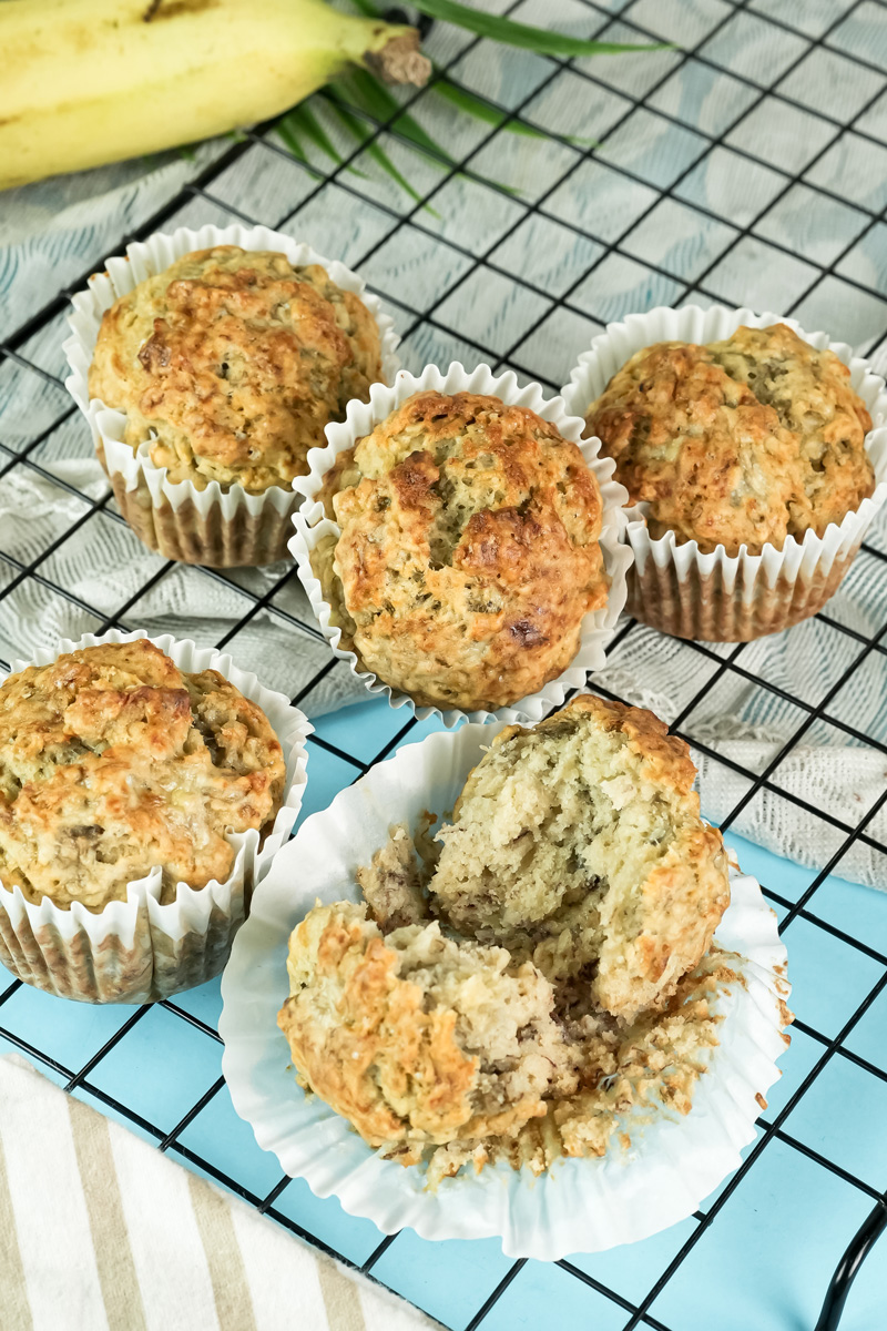 A whole and a halved banana protein muffin on a cooling rack, showing the texture