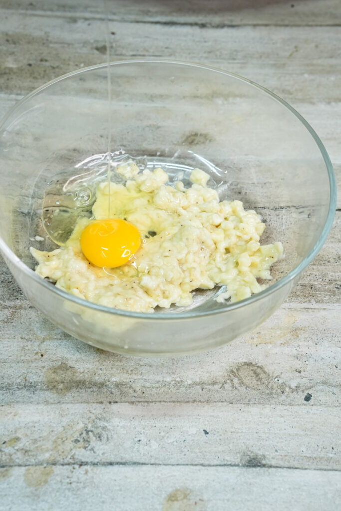 A whole egg and a mashed banana mixture in a clear glass bowl, preparing to be mixed