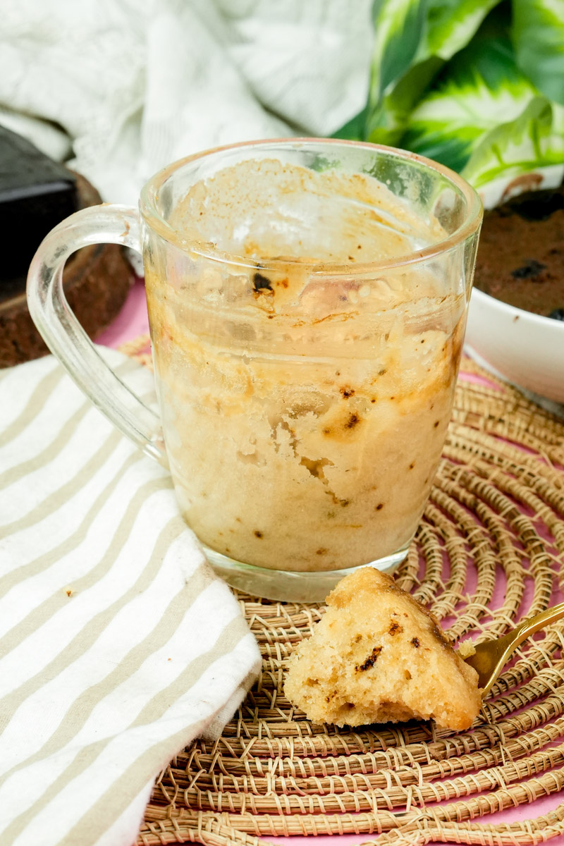 A bite of coffee mug cake resting on a woven coaster next to the mug