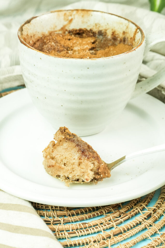 A bite of snickerdoodle mug cake resting on a white plate next to the mug