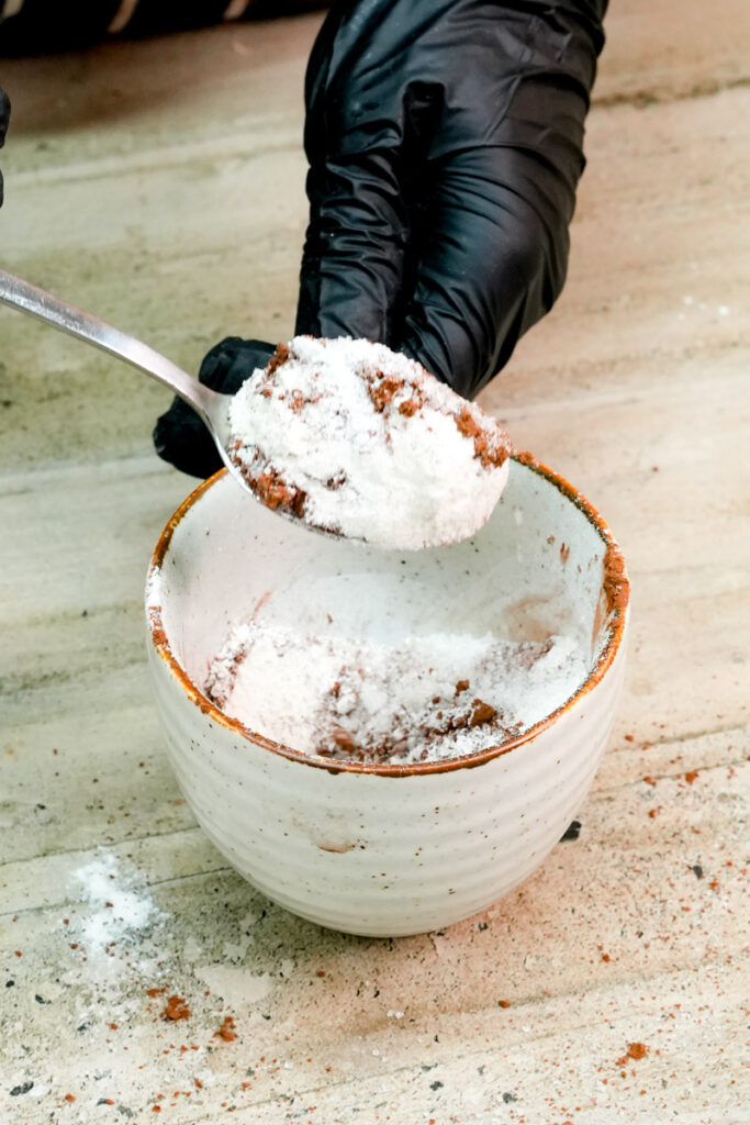 A spoonful of dry mug cake mix being added to a ceramic mug