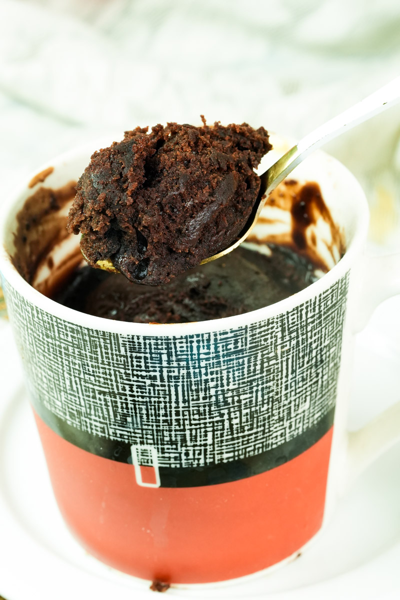 A spoonful of fluffy, cooked chocolate vegan mug cake held over the mug