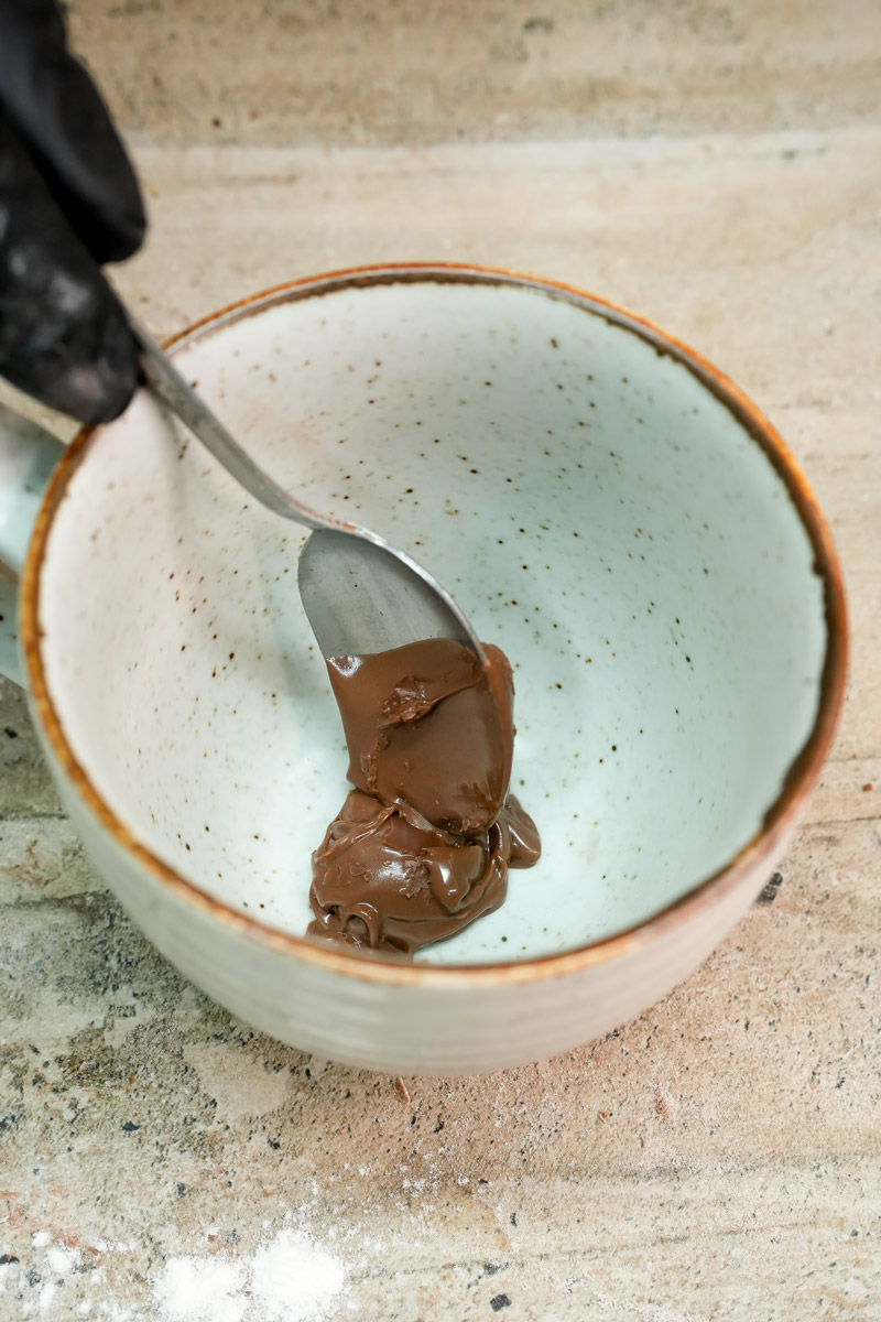 Adding a large spoonful of Nutella hazelnut spread into a white ceramic mug