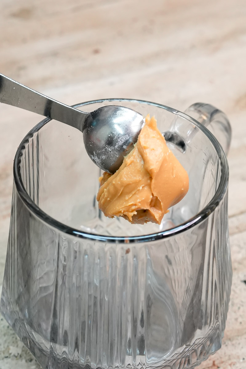 Adding a scoop of creamy peanut butter into a glass mug