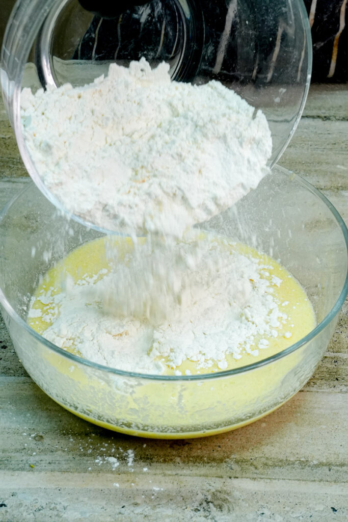 Adding all-purpose flour to the wet ingredients in a clear bowl