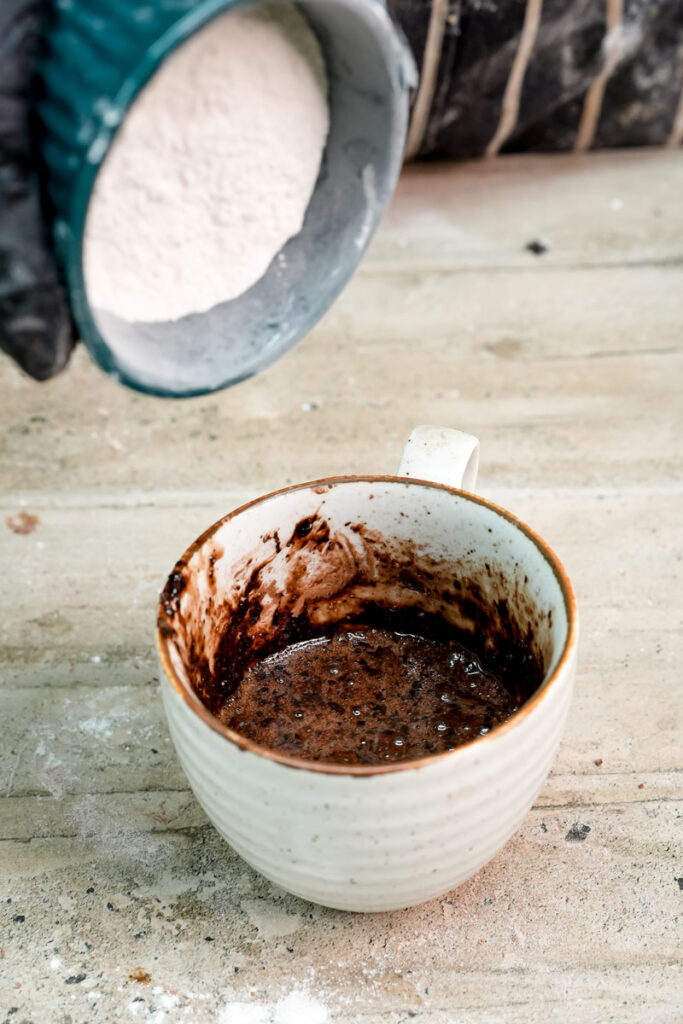 Adding all-purpose flour to the wet chocolate cake batter in the mug