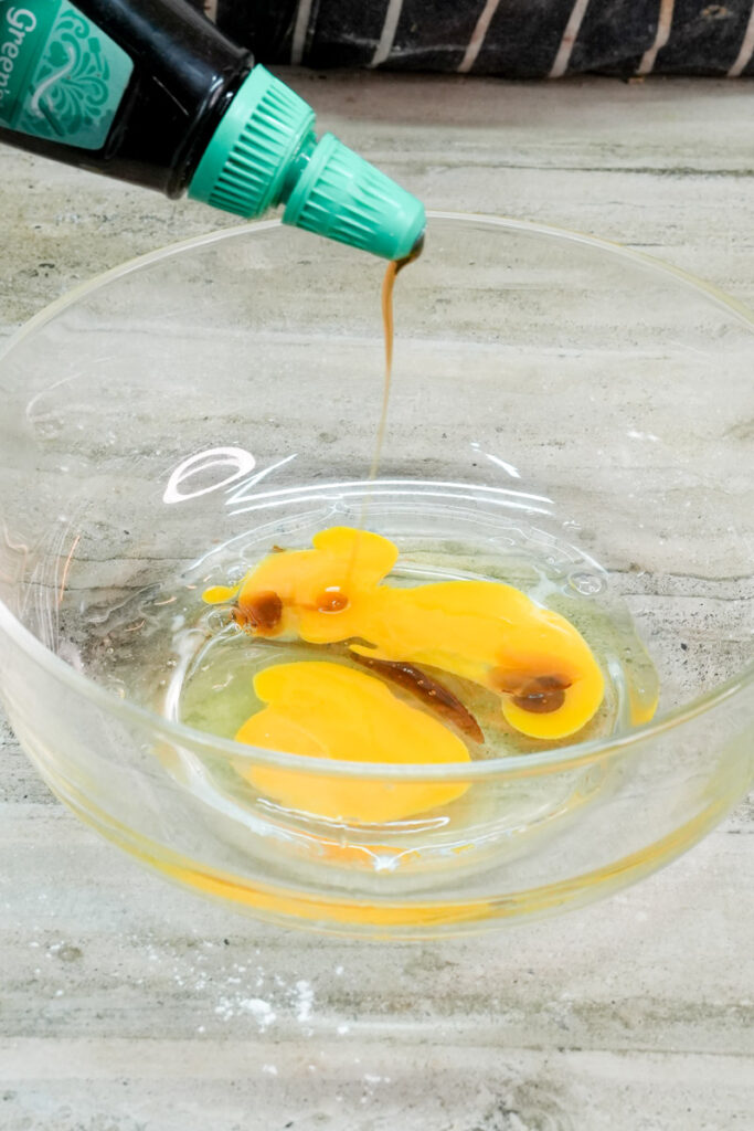 Adding maple syrup to eggs in a glass mixing bowl
