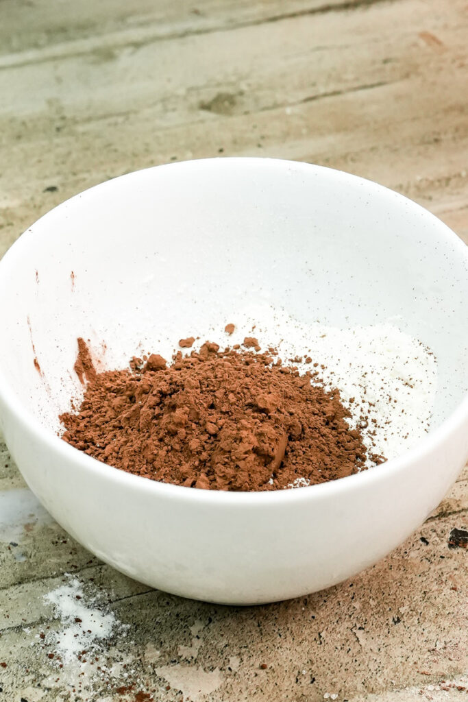 Combining flour and cocoa powder in a white bowl for a healthy mug cake recipe