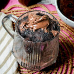 Finished keto mug cake with creamy hazelnut topping on a pink background