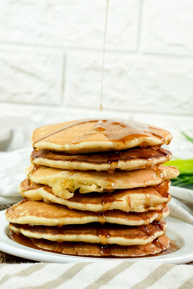 Fluffy American pancakes on a plate with maple syrup being poured over.
