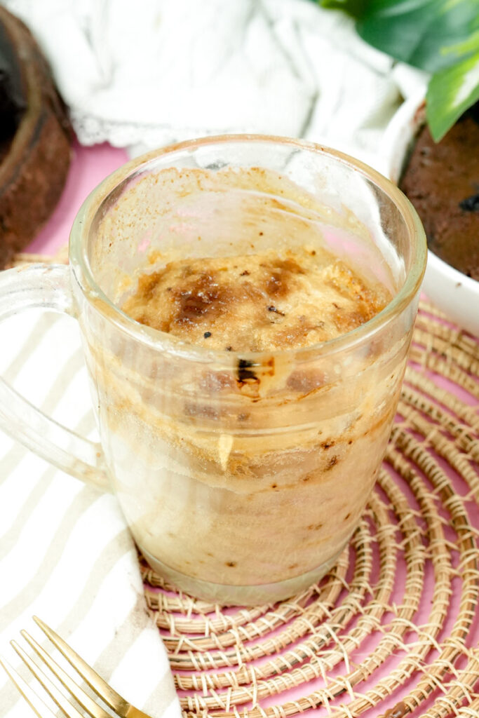 Freshly baked coffee mug cake in a clear glass mug on a pink background