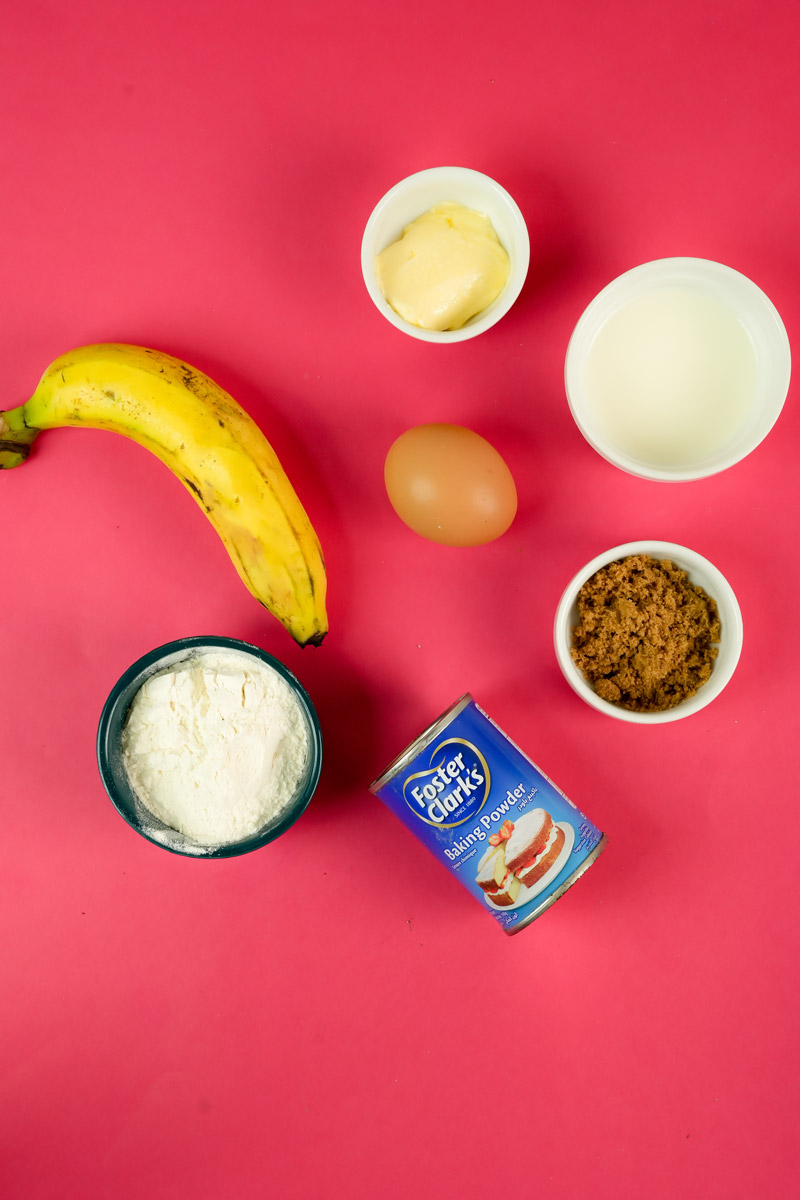 Ingredients for banana mug cake including a banana, egg, flour, milk, butter, brown sugar, and baking powder