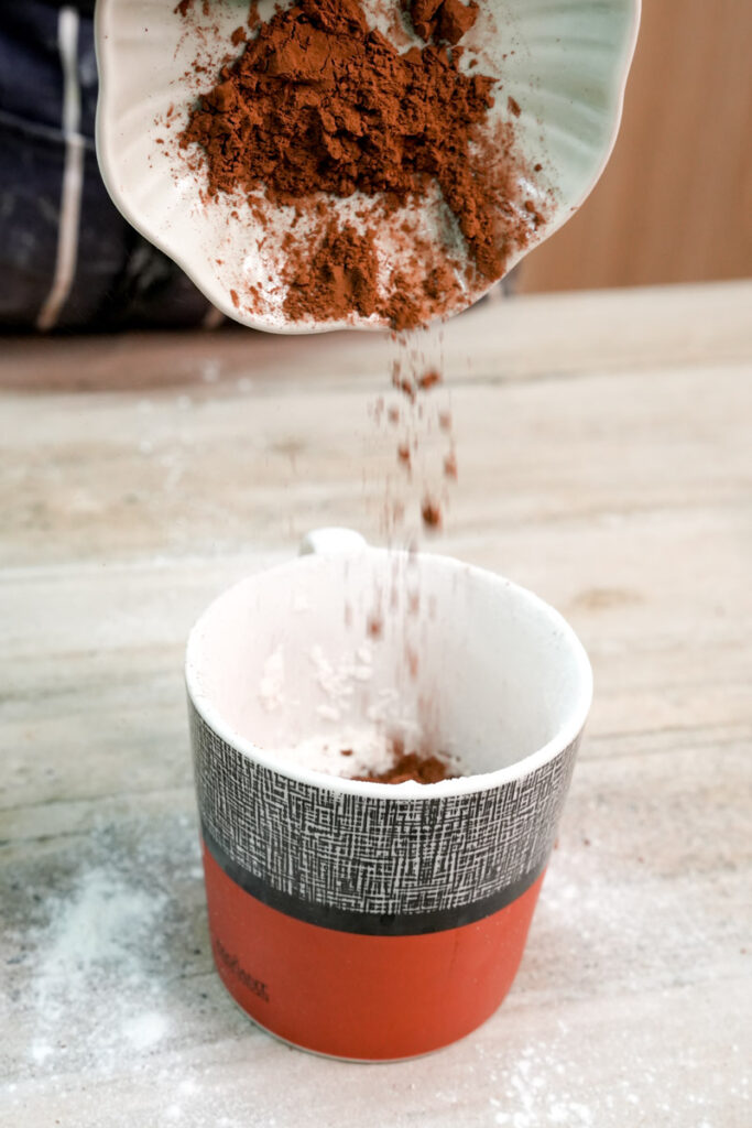 Pouring cocoa powder into a mug for a vegan dessert