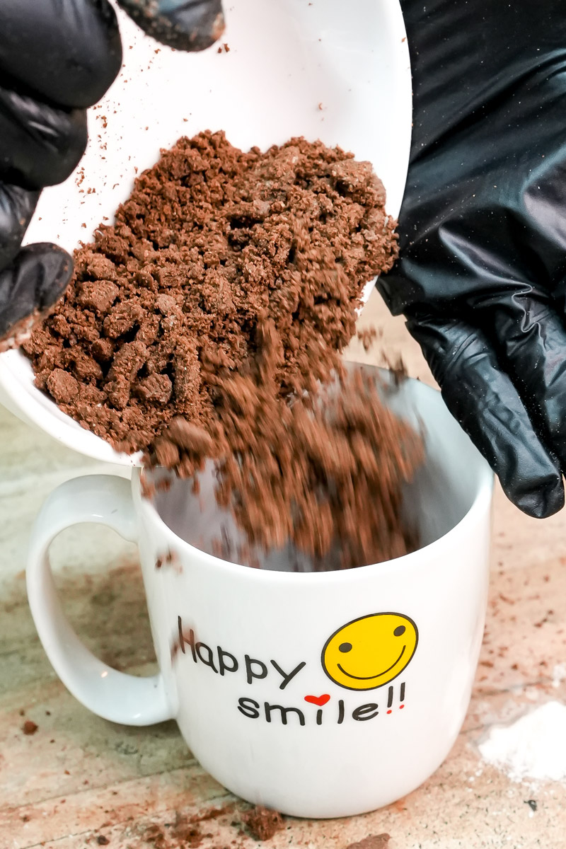 Pouring crushed Oreo cookies into a white ceramic mug