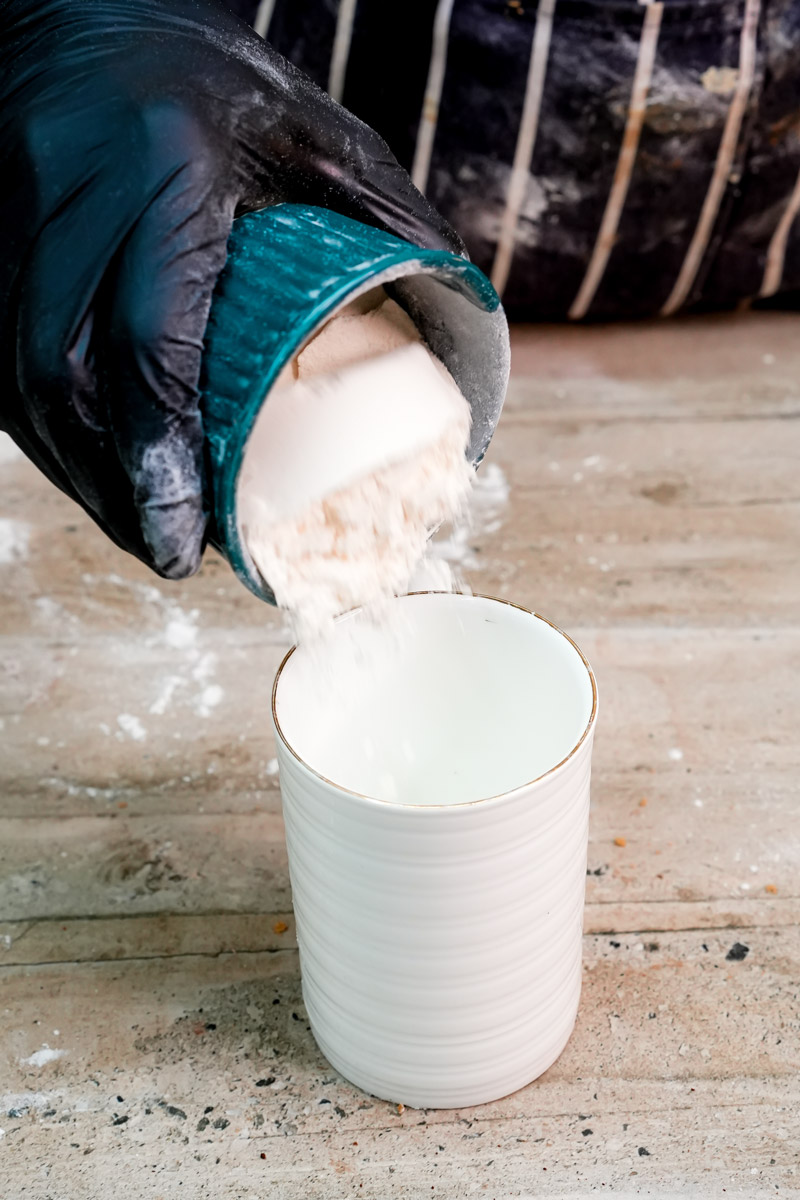Pouring dry ingredients into a white mug for a protein cake
