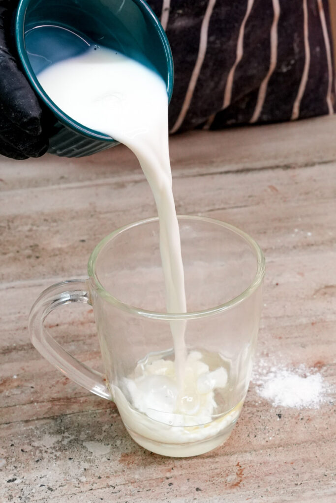 Pouring milk into a glass mug for chocolate mug cake batter