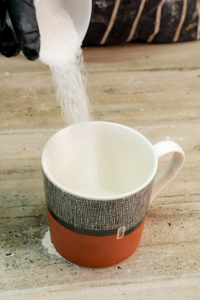 Pouring sugar into a mug for a microwave chocolate cake recipe