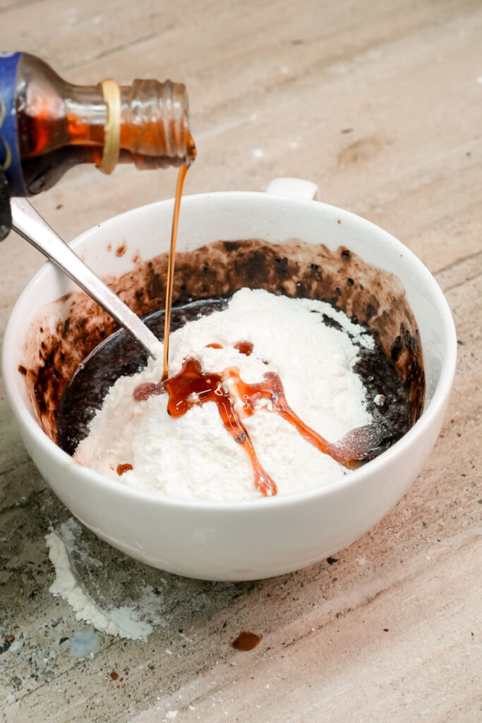 Pouring vanilla extract over the mug cake dry ingredients