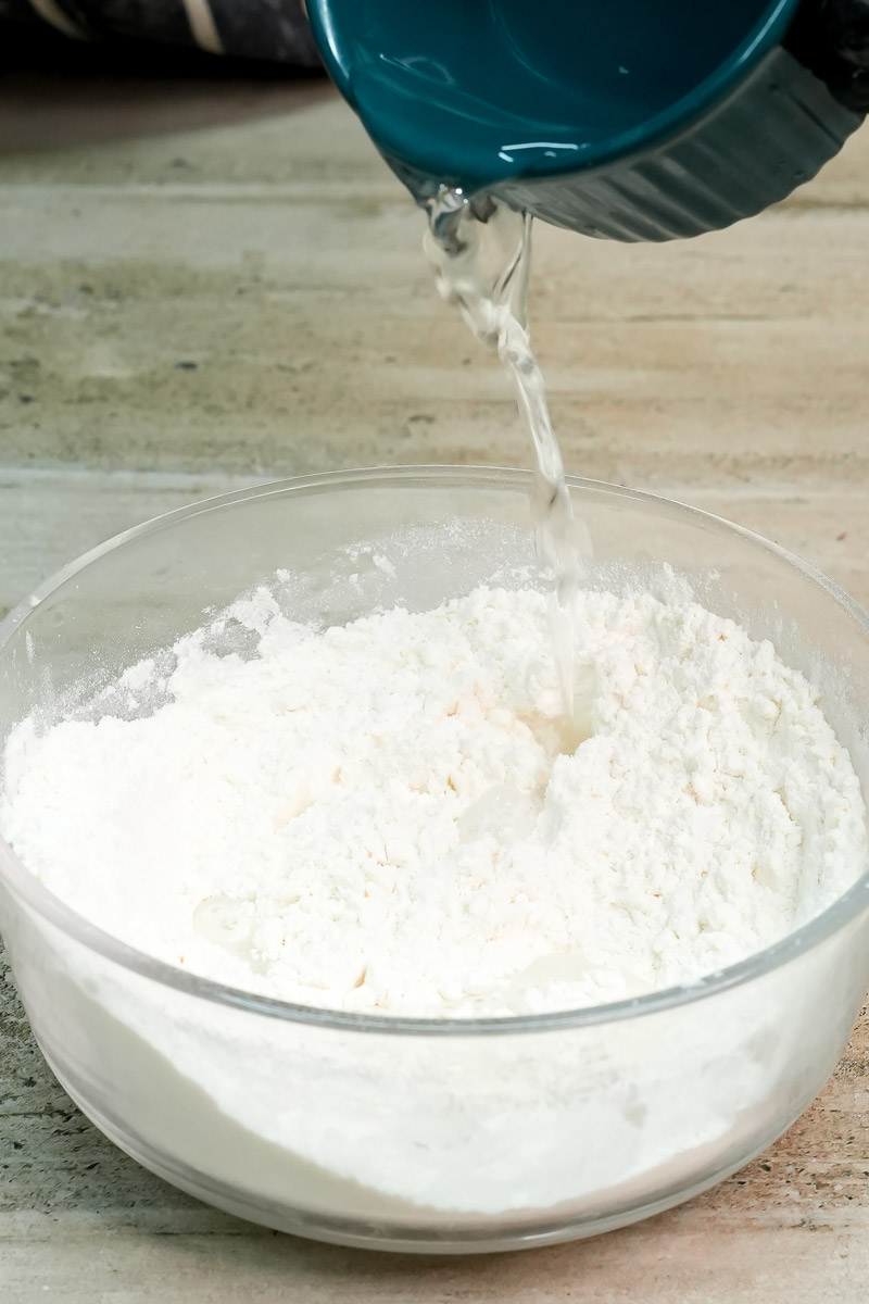 Pouring water into a bowl of flour to make cinnamon roll dough