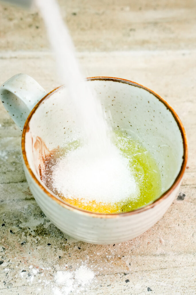 Pouring white granulated sugar into the mug cake mixture