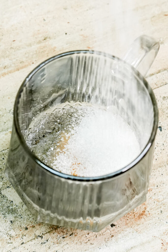 Pouring white granulated sugar into a mug for peanut butter cake batter