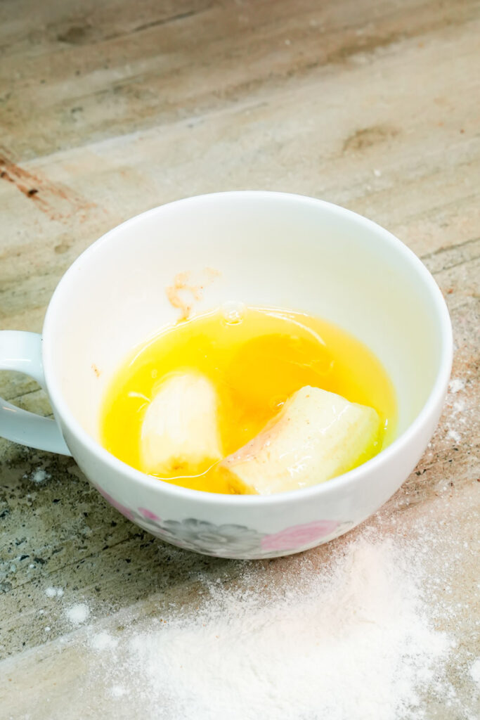 Raw egg added to banana pieces in a mug for cake batter