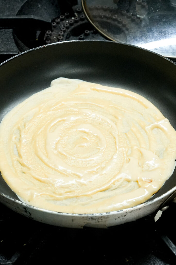 Spreading thin pancake batter in a hot skillet to cook