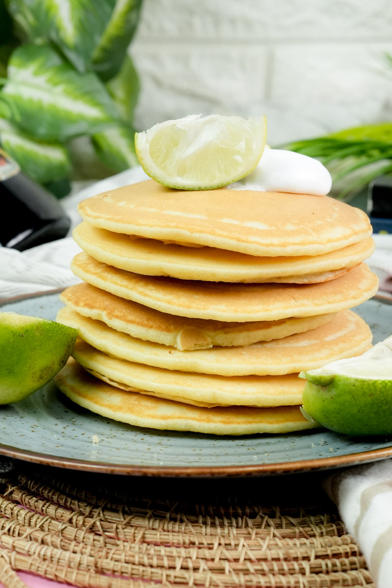 Stack of fluffy lemon pancakes topped with whipped cream and a fresh lime wedge