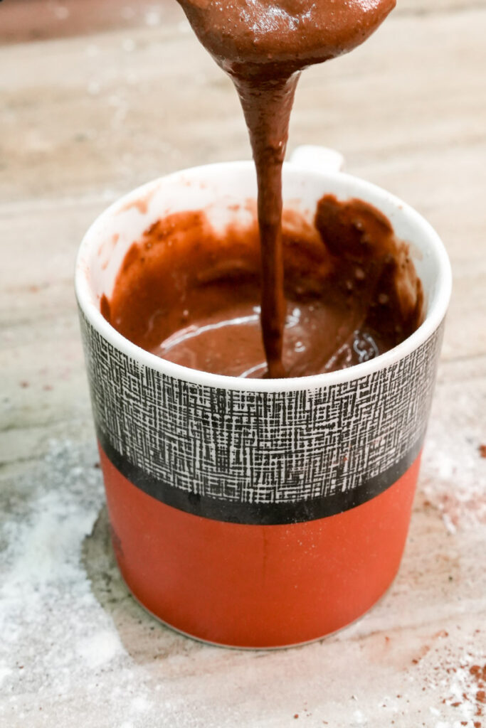 Thick and glossy chocolate mug cake batter dripping from a spoon into a mug