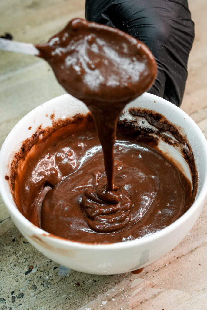 Thick chocolate mug cake batter dripping from a spoon into a cup