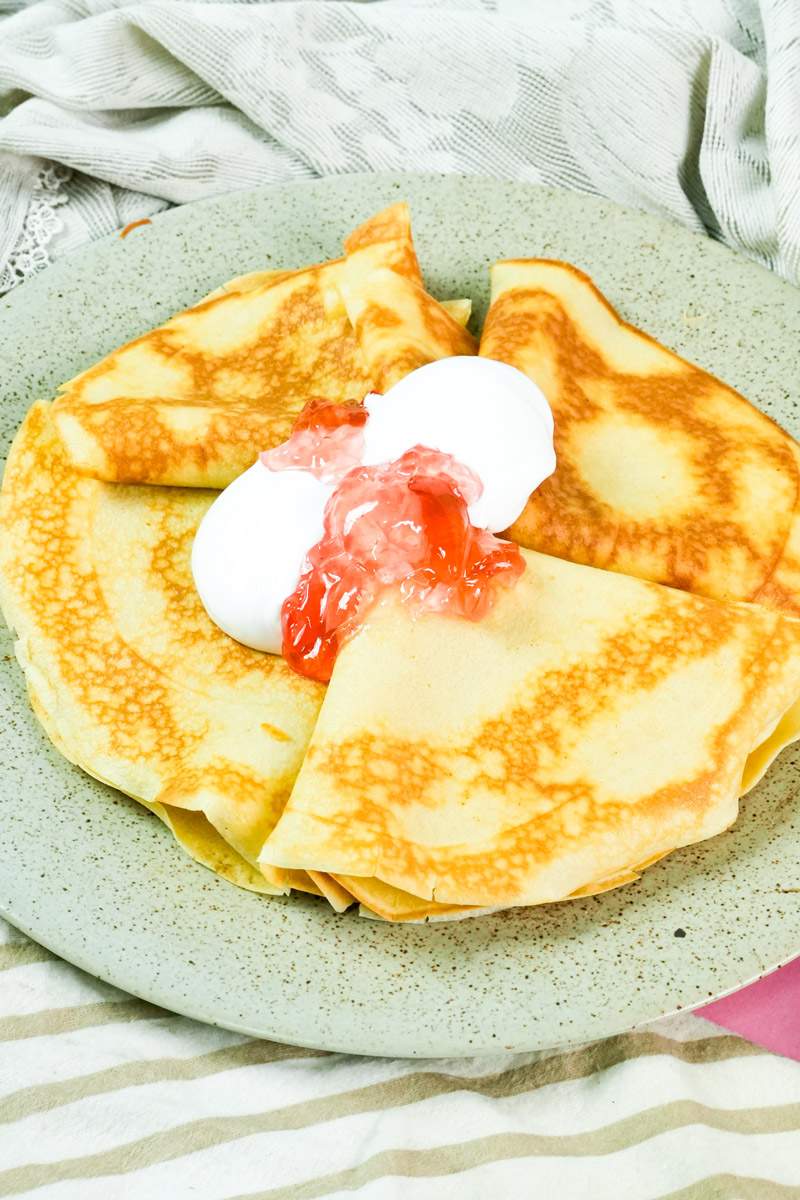 Traditional Russian blini served with a dollop of white cream and red preserve