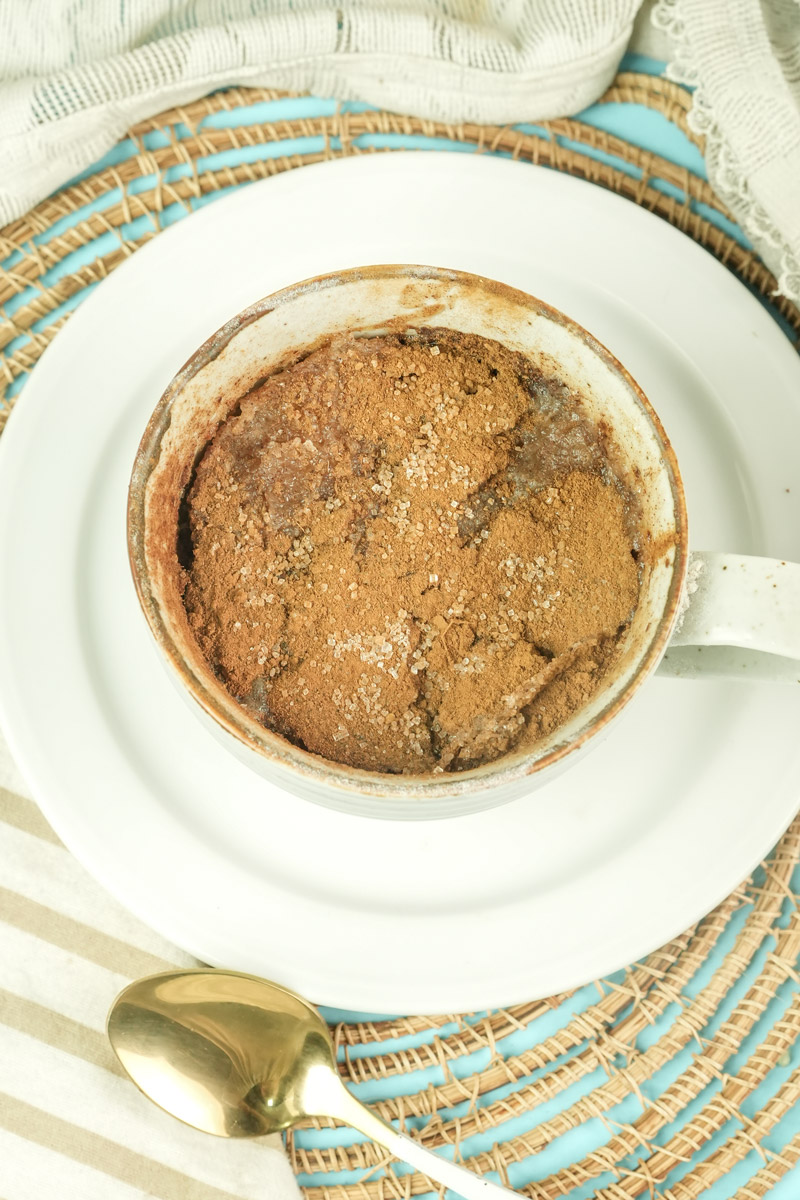 Top-down view of a finished snickerdoodle mug cake on a white plate with a gold spoon