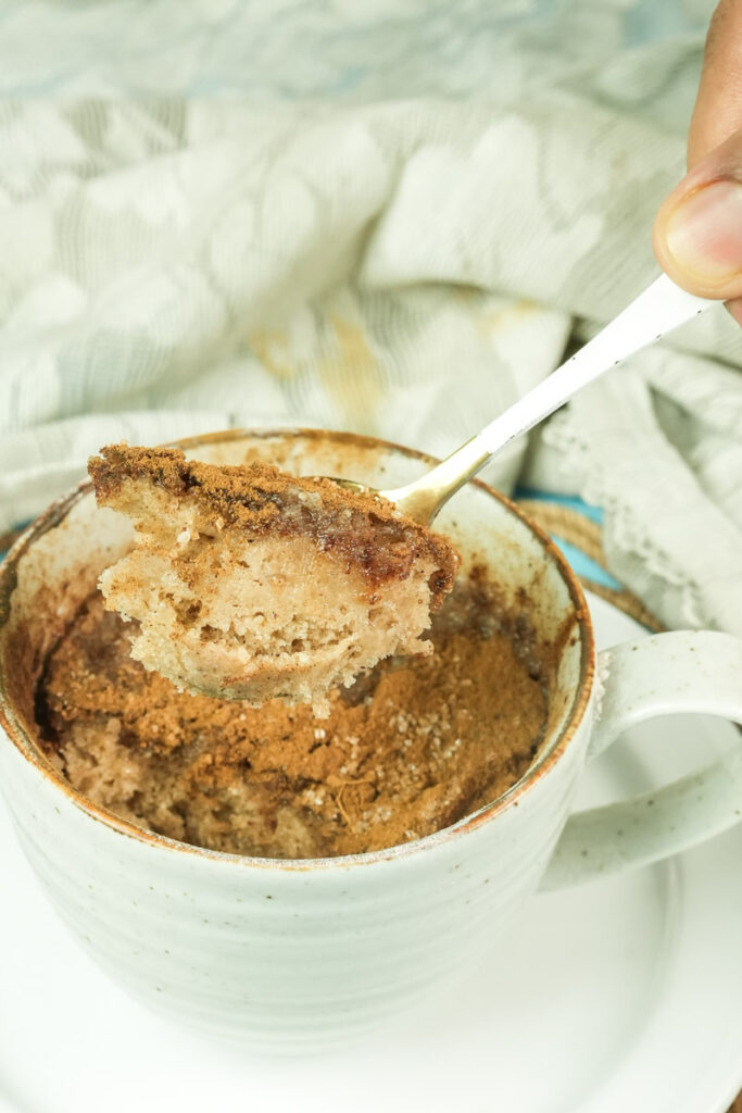 A spoon lifting a fluffy bite of warm cinnamon snickerdoodle mug cake