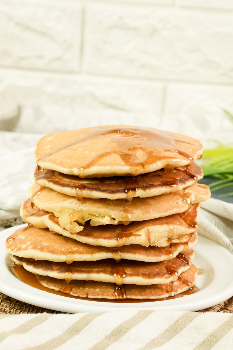 A stack of golden brown American pancakes soaked in breakfast syrup.