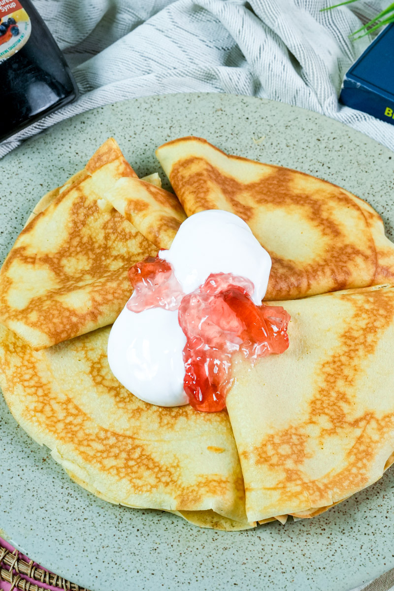 Pouring maple syrup over a stack of Russian pancakes