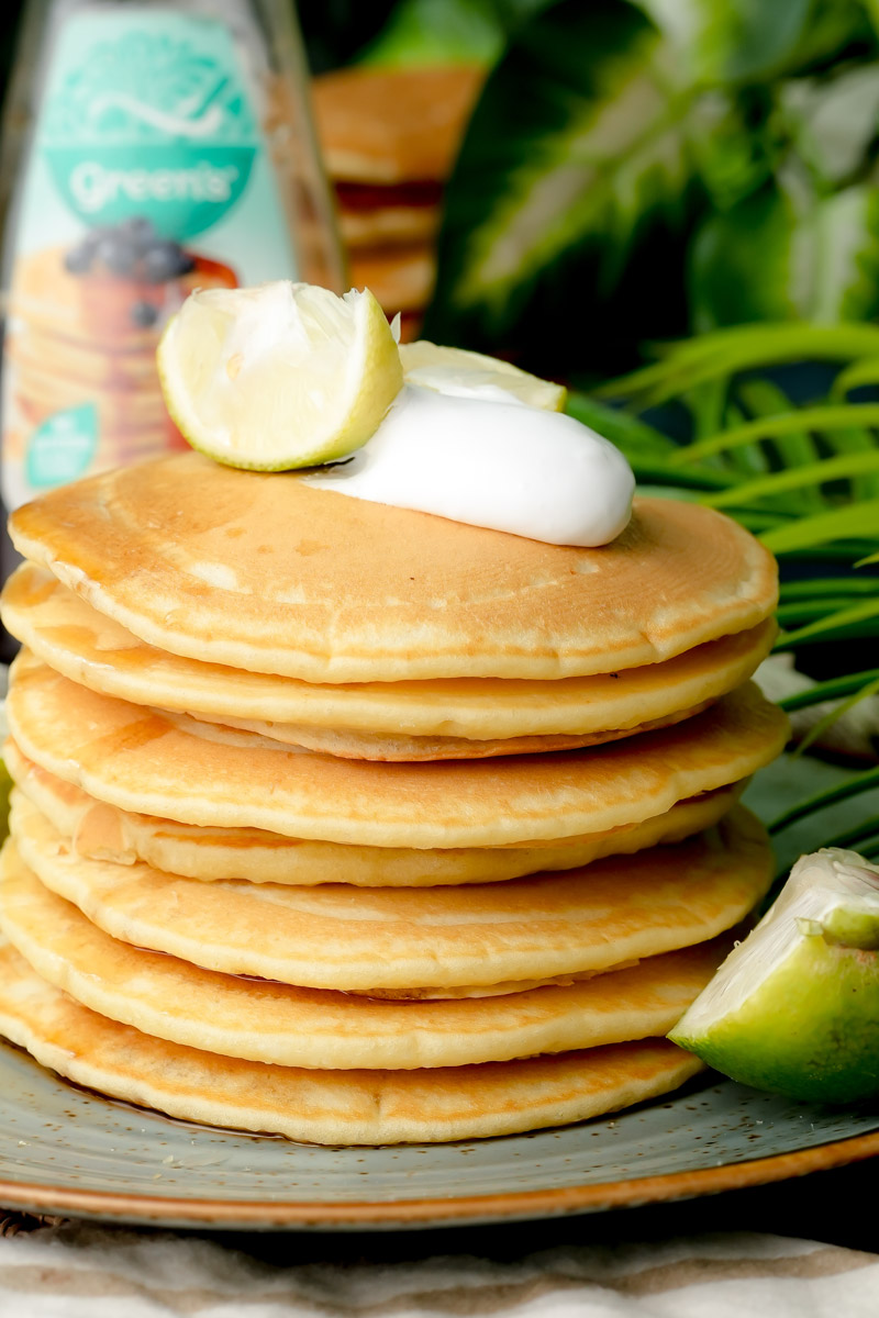 Side view of a thick stack of pancakes with maple syrup bottle in the background