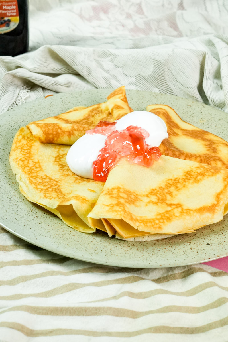A plate of thin crepes topped with sweet jam and thick cream, close-up view