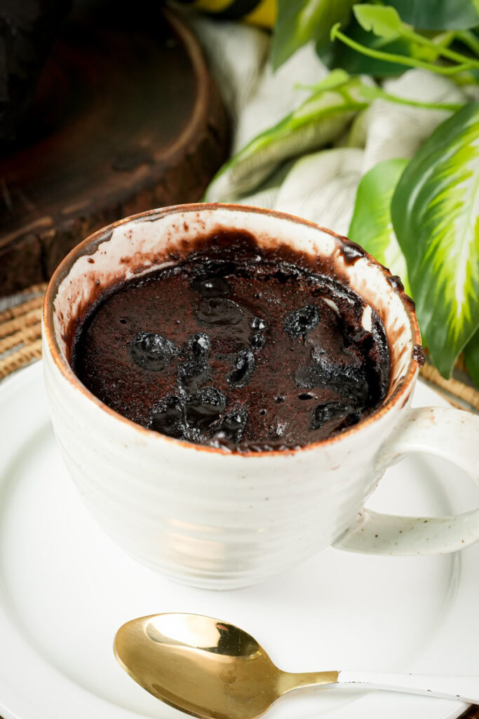 Close up of a warm chocolate brownie in a mug with a gold spoon